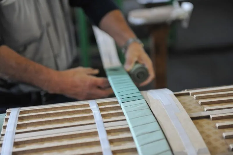 Craftsman installing turquoise fretboard on wooden guitar neck during instrument assembly